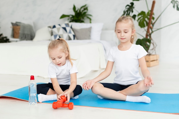 Vue de face des filles exerçant à la maison sur un tapis de yoga