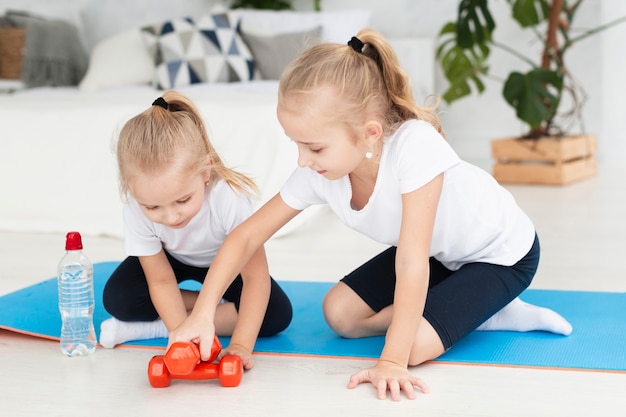 Vue de face des filles à la maison sur un tapis de yoga avec des poids