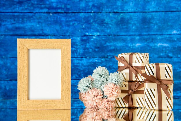 Vue de face des fleurs de cadre photo de cadeaux de vacances reflétées sur un miroir sur fond de bois bleu