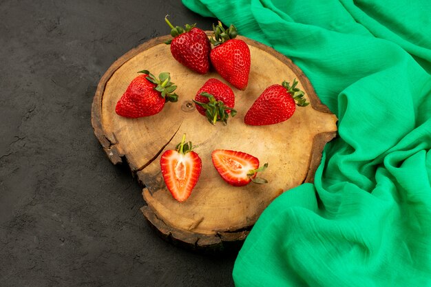 vue de face fraises fraîches mûres rouges mûres tranchées et entières sur le bureau en bois brun sur le gris