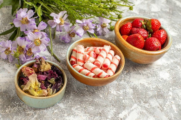 Vue de face fraises rouges fraîches avec des fleurs sur la surface blanche des fruits de baies de bonbons rouges