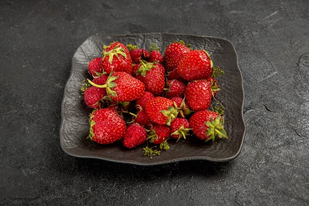 Vue de face fraises rouges fraîches à l'intérieur de la plaque sur fond sombre