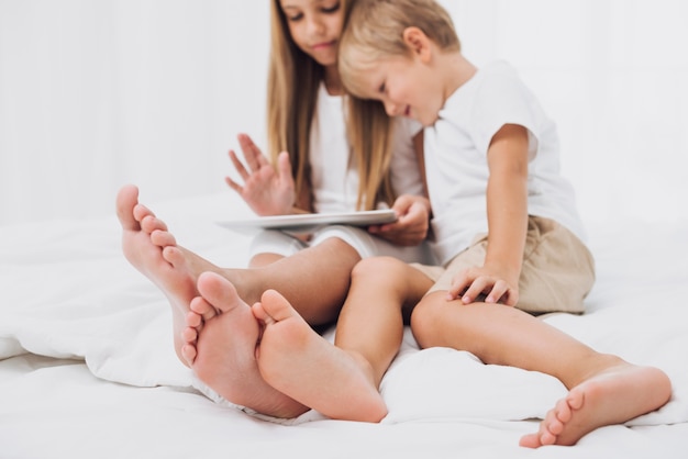 Vue de face des frères et sœurs restant au lit tout en regardant leur tablette