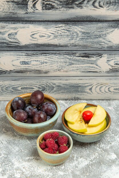 Vue de face fruits frais prunes framboises et pommes sur fond gris fruits mûrs moelleux frais