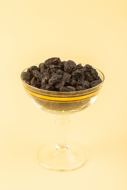 Une vue de face fruits secs noirs aigre séché à l'intérieur peu de verre transparent isolé sur le fond de couleur crème fruits noirs secs