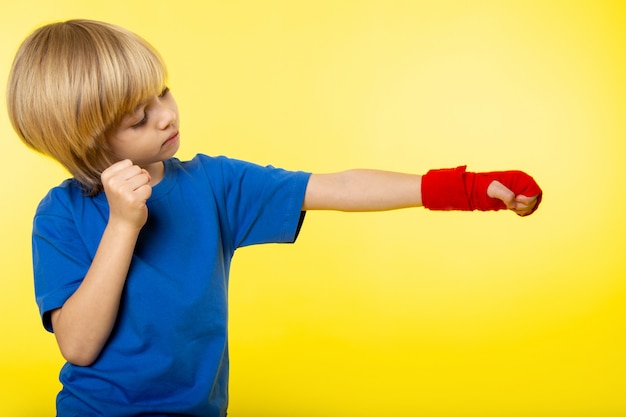 Une vue de face garçon blond posant la boxe en t-shirt bleu sur le mur jaune