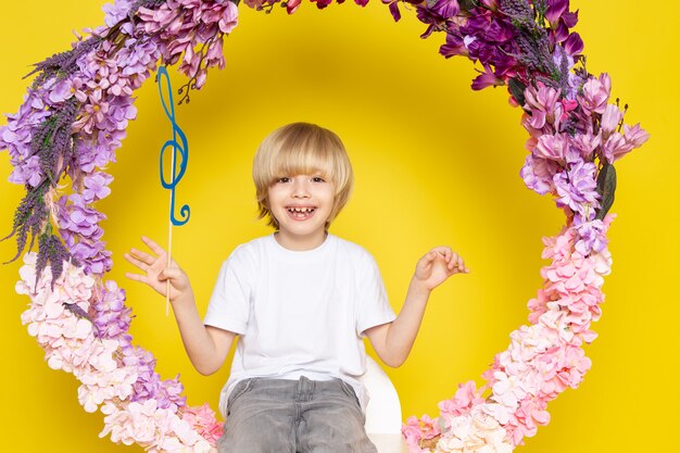 Une vue de face garçon blond souriant en t-shirt blanc assis sur la fleur fait stand sur le bureau jaune