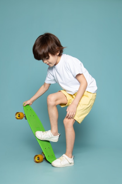 Une vue de face garçon souriant en t-shirt blanc équitation planche à roulettes sur le backgorund bleu