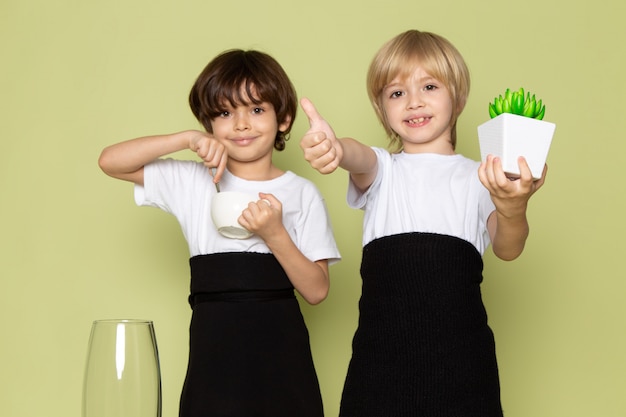 Une vue de face garçons cute smiling holding green petite plante et café sur le sol de couleur pierre