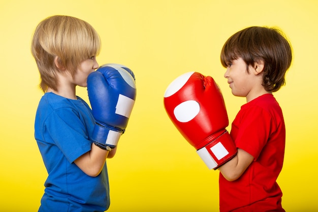 Une vue de face garçons face à face dans des gants de boxe de couleur différente et des t-shirts sur le mur jaune