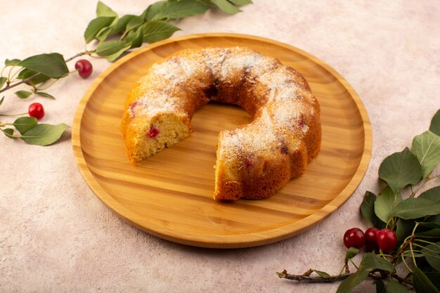 Une vue de face gâteau aux fruits cuit délicieux en tranches avec des cerises rouges à l'intérieur et du sucre en poudre sur un bureau rond en bois sur rose