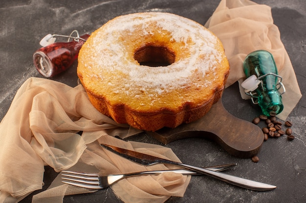 Une vue de face gâteau rond cuit avec du sucre en poudre et des graines de café sur le bureau en bois