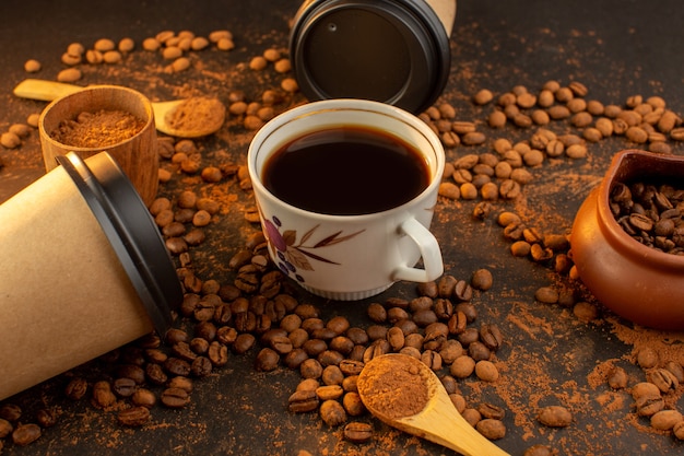 Une vue de face des graines de café brun avec des barres de chocolat et une tasse de café sur toute la surface sombre et granule de grain de café