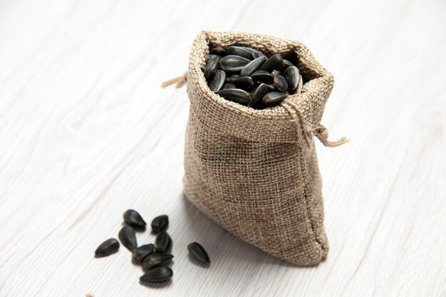 Vue de face graines de tournesol fraîches graines de couleur noire à l'intérieur d'un petit sac sur fond blanc photo de collation de graines beaucoup d'huile
