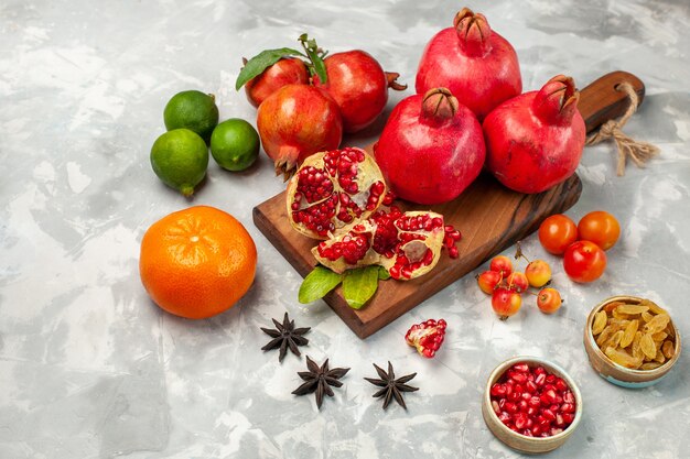 Vue de face des grenades rouges fraîches avec des mandarines et des prunes sur le bureau blanc clair