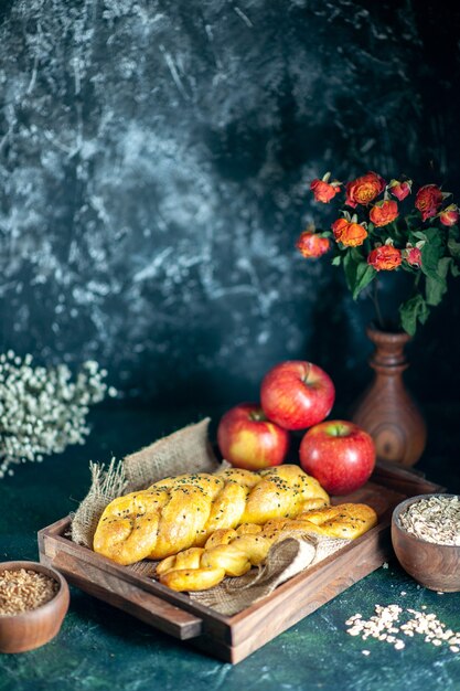 Vue de face de gressins torsadés pommes sur planche de bois rectangle avoine et grains de blé dans des bols