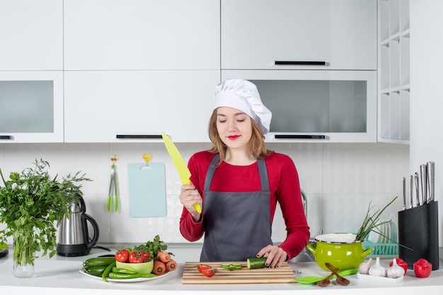 Vue de face heureuse femme cuisinier en tablier tenant un couteau