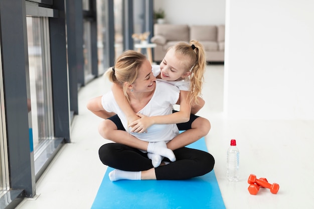 Vue de face de l'heureuse mère et l'enfant sur un tapis de yoga avec des poids