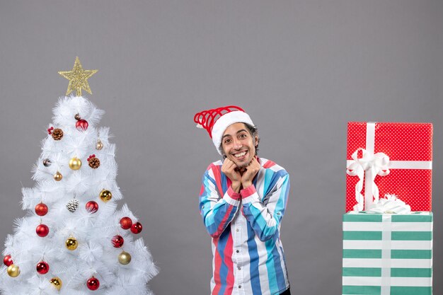 Vue de face heureux beau mec mettant les mains sur son visage près de l'arbre de Noël blanc