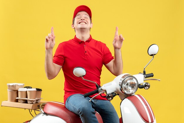 Vue de face de l'heureux jeune homme portant chemisier rouge et chapeau livrant des commandes pointant vers le haut sur fond jaune