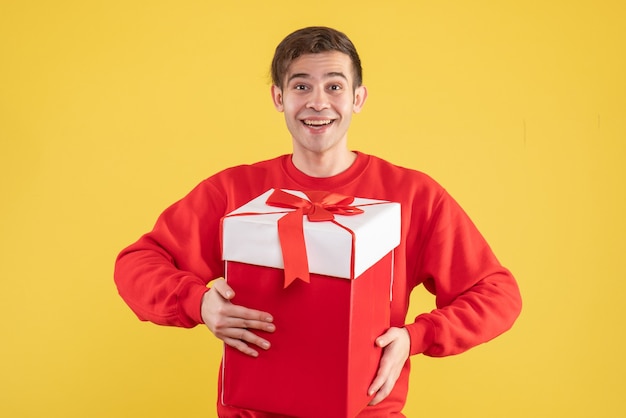 Vue de face heureux jeune homme avec pull rouge debout sur jaune