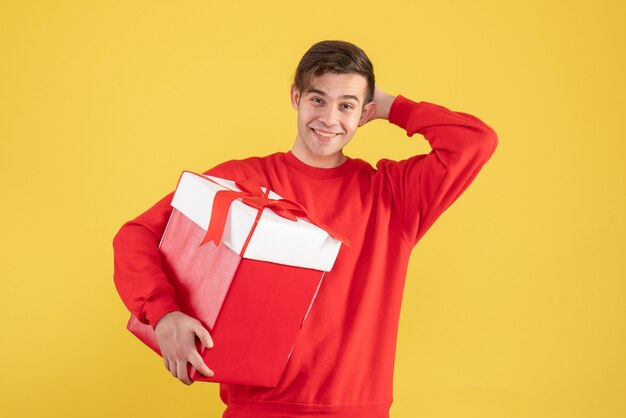 Vue de face heureux jeune homme avec pull rouge debout sur jaune