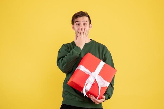 Vue de face heureux jeune homme avec pull vert debout sur jaune