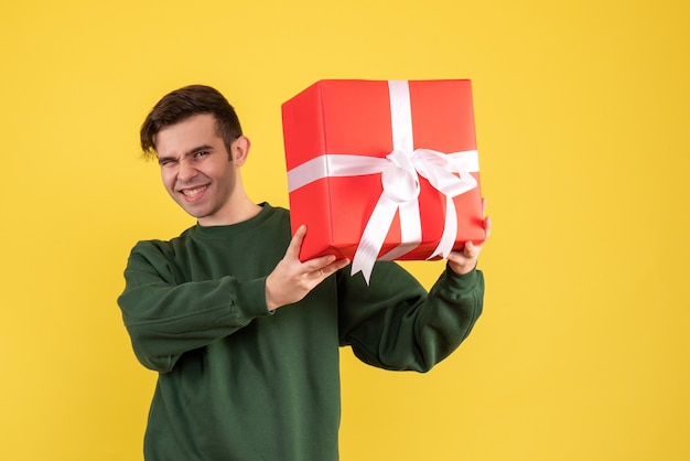 Vue de face heureux jeune homme avec pull vert debout sur jaune