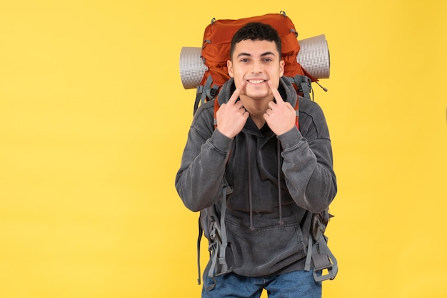 Vue de face heureux jeune homme avec sac à dos rouge pointant sur son sourire