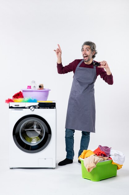 Vue de face heureux jeune homme tenant une carte debout près de la machine à laver sur fond blanc isolé