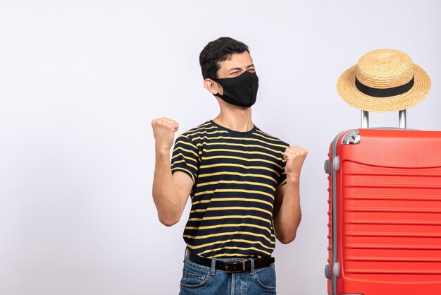 Vue de face heureux jeune touriste avec masque noir debout près de valise rouge