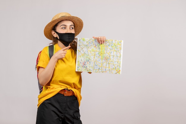 Photo gratuite vue de face de l'heureux jeune voyageur avec sac à dos tenant la carte sur le mur gris