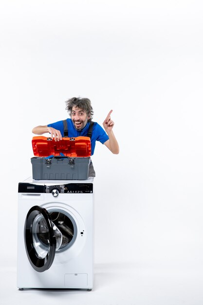 Vue de face heureux réparateur ouvrant le sac à outils derrière une machine à laver blanche sur un espace blanc
