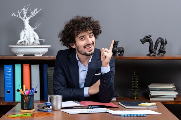 Vue de face homme d'affaires aux cheveux bouclés surprenant avec une idée assis au bureau dans un bureau moderne