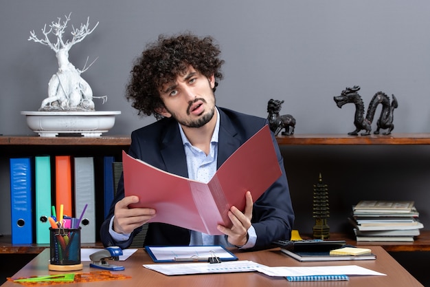 Vue de face homme d'affaires confus assis au bureau avec des papiers dans son bureau