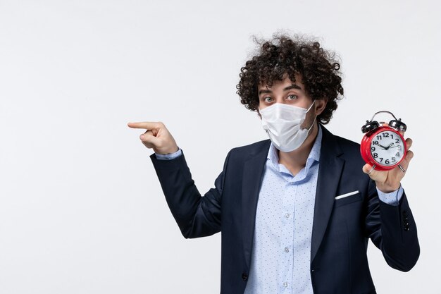 Vue de face d'un homme d'affaires en costume et portant son masque tenant une horloge pointant quelque chose sur le côté droit