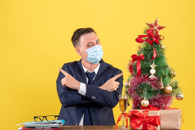 Vue de face homme d'affaires croisant les mains assis à la table près de l'arbre de Noël et présente sur fond jaune