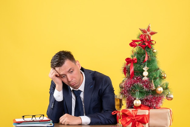 Vue de face de l'homme d'affaires déprimé assis à la table près de l'arbre de Noël et présente sur jaune