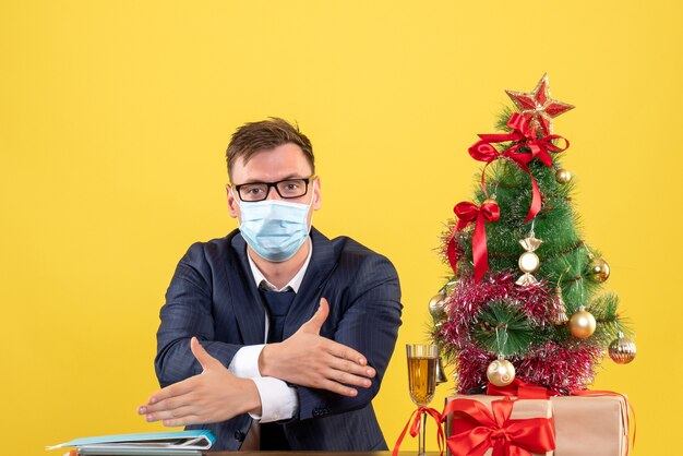 Vue de face de l'homme d'affaires donnant les mains assis à la table près de l'arbre de Noël et présente sur jaune