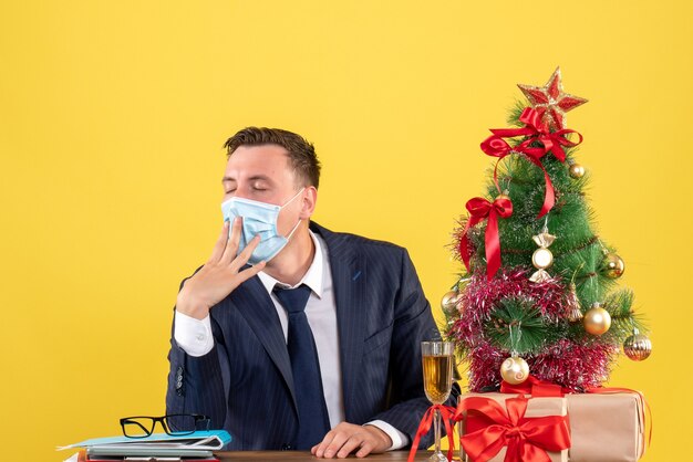 Vue de face de l'homme d'affaires endormi assis à la table près de l'arbre de Noël et présente sur jaune