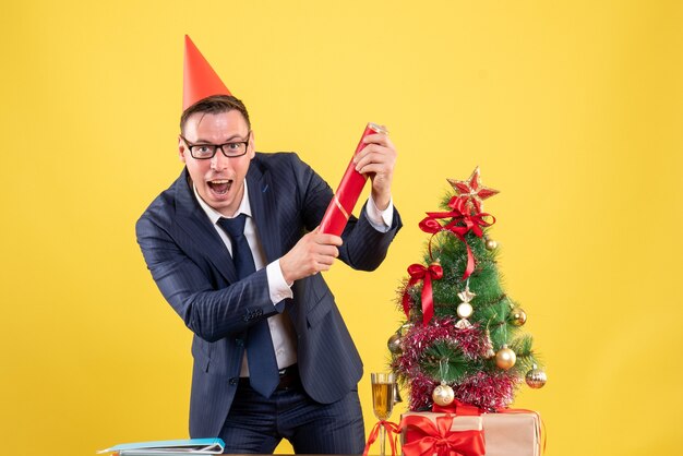 Vue de face de l'homme d'affaires réjoui debout près de l'arbre de Noël et présente sur jaune