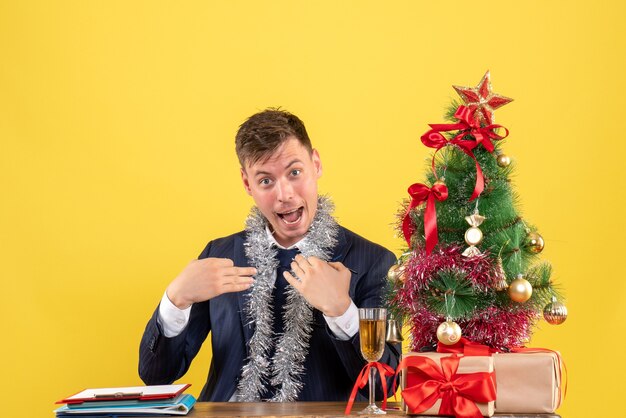 Vue de face de l'homme d'affaires se montrant assis à la table près de l'arbre de Noël et présente sur jaune