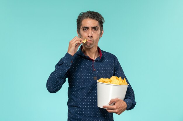 Vue de face homme d'âge moyen avec panier plein de cips sur surface bleu clair