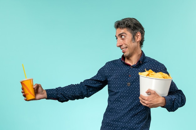 Vue de face homme d'âge moyen tenant des cips de pommes de terre et de la soude sur une surface bleu clair