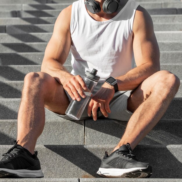 Vue de face homme assis dans les escaliers tout en tenant une bouteille d'eau