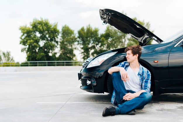 Vue de face d'un homme assis près d'une voiture