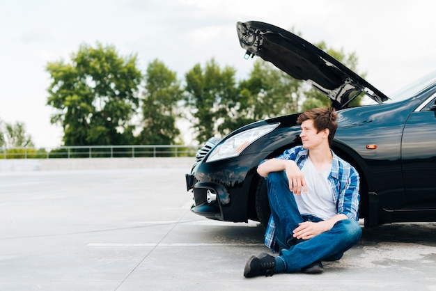 Vue de face d'un homme assis près d'une voiture