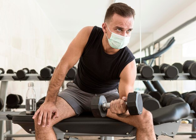 Vue de face de l'homme au gymnase avec masque médical travaillant