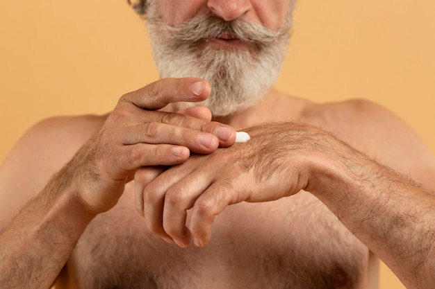 Vue de face de l'homme barbu senior appliquant la crème