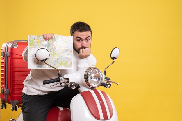 Vue de face d'un homme concentré assis sur une moto avec une valise dessus tenant une carte sur fond jaune isolé